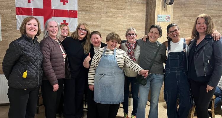 Glimlachende groep vrouwen die binnenshuis poseren met een Georgische vlag die aan de muur achter hen hangt.