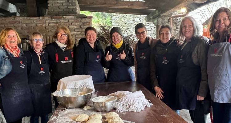 Deelnemers in schorten staan rond een rustieke tafel met deeg en kommen tijdens een Georgische kookles.