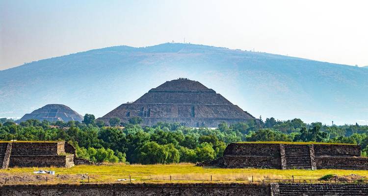 Fernblick auf die Sonnenpyramide, eingerahmt von grünem Wald mit Bergen im nebligen Hintergrund in Teotihuacán.