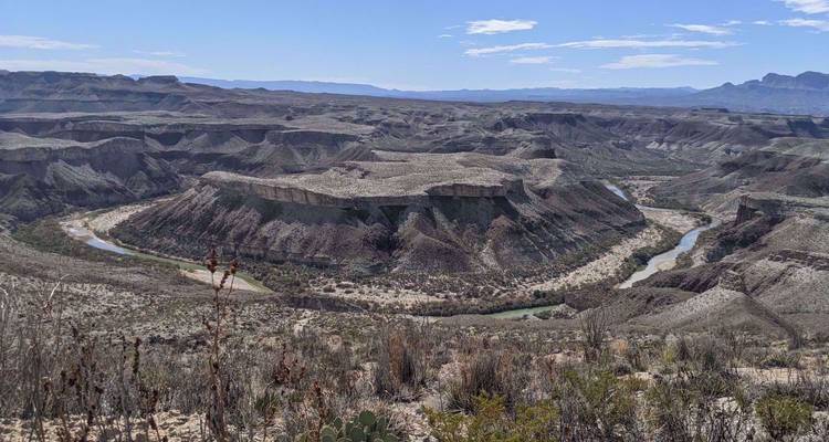 Canyon désertique aux vastes étendues avec une rivière sinueuse bien en dessous sous un soleil de midi éclatant