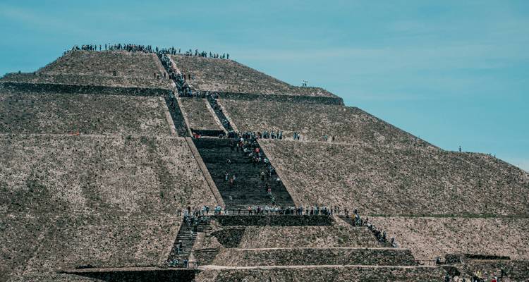 Teleaufnahme von Besuchern, die die steilen Stufen der Teotihuacán-Pyramide vor blauem Himmel erklimmen.
