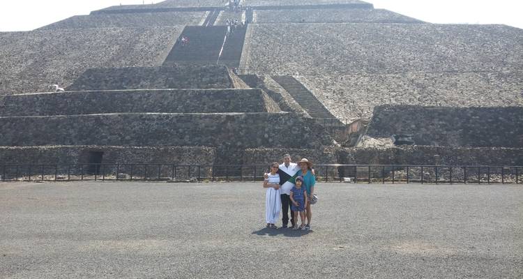 Familie steht auf weitem Platz vor massiver Pyramidenstruktur unter der grellen Mittagssonne.
