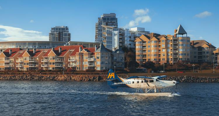 Een Harbour Air watervliegtuig taxiet over rustig havenwater voor moderne waterfront appartementen.