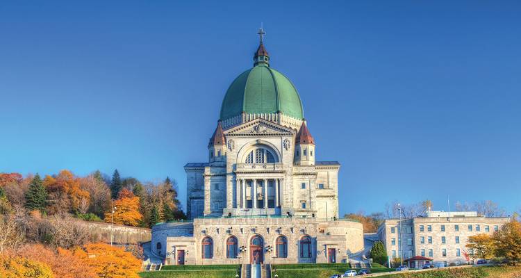 La grande basilique de l'Oratoire Saint-Joseph s'élève contre un ciel bleu clair avec un feuillage automnal vibrant à sa base.