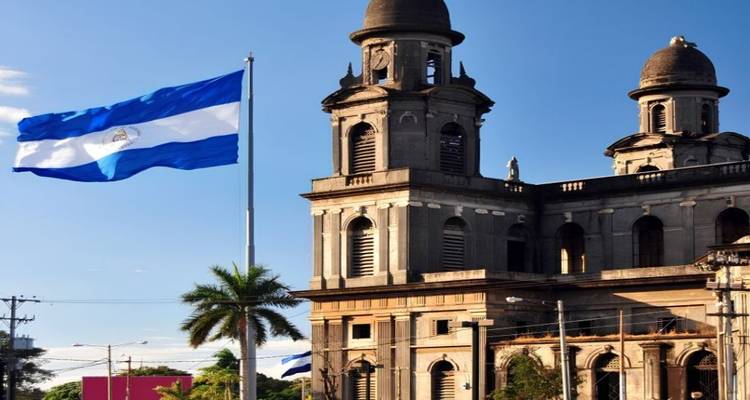 Nicaraguaanse vlag wappert naast de historische stenen kathedraalruïnes van Managua verlicht door late middagzon.