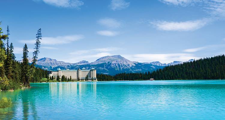 Het historische Fairmont Chateau weerspiegeld in het rustige turquoise water van Lake Louise, omgeven door dennenbos.
