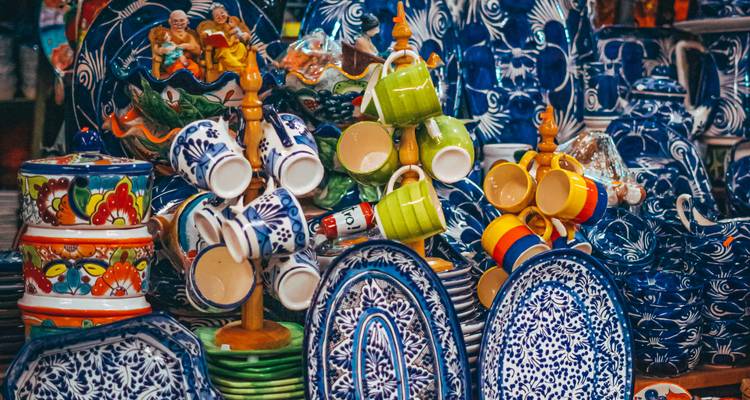 Ausstellung von bunt bemalter Talavera-Keramik und gestapelten Keramikbechern auf einem Kunsthandwerkermarkt.