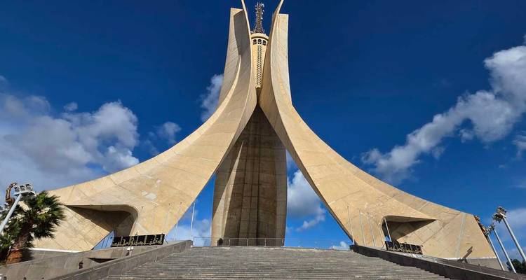 Dramatic upward view of the Martyrs' Memorial monument against a bright blue sky with scattered clouds.