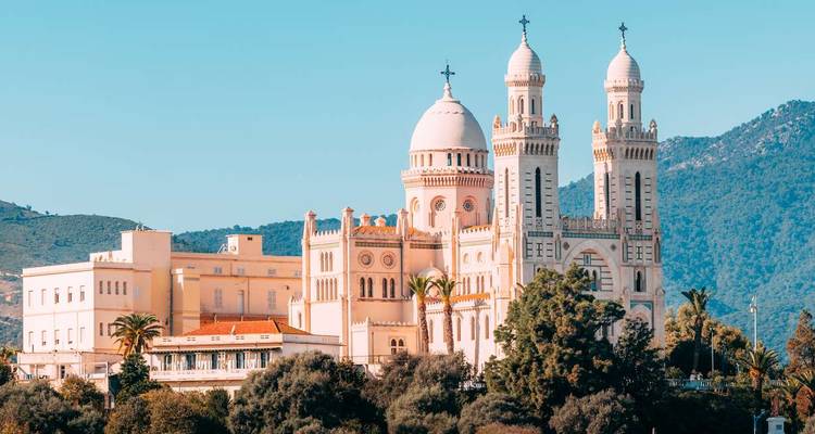 Elegant basilica with twin towers and dome set against green hills and a clear sky.