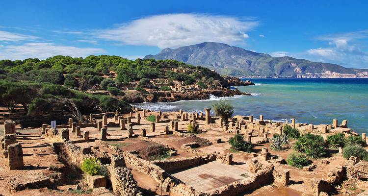 Coastal Roman ruins overlooking turquoise sea with mountains in the background.