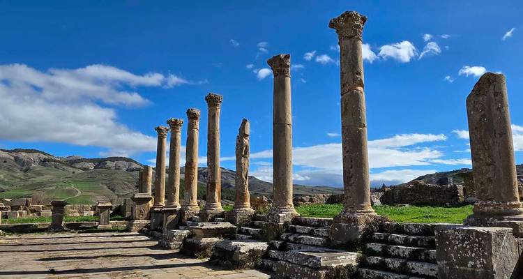 Row of standing Roman columns on a stone platform with rolling hills under blue sky.