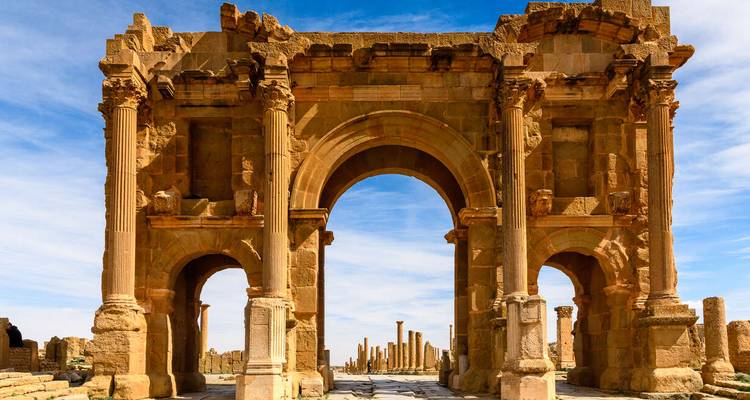 Well-preserved Roman arch with columns and intricate carvings under a bright sky.