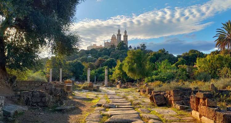 Stone pathway through lush ruins leading to a hilltop basilica under soft afternoon light.