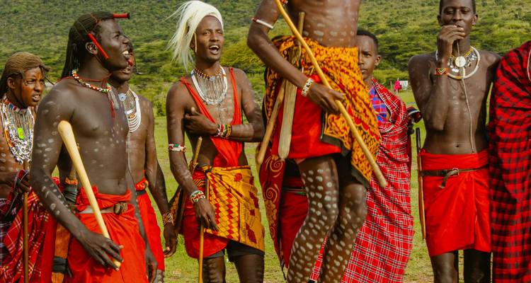 Groupe de guerriers Maasaï en tenue colorée exécutant une danse traditionnelle avec des sauts.
