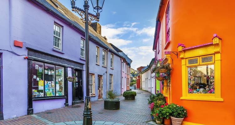 Charmante schmale Gasse gesäumt von bunt bemalten Ladenfronten und Blumen in Kinsale, Irland.