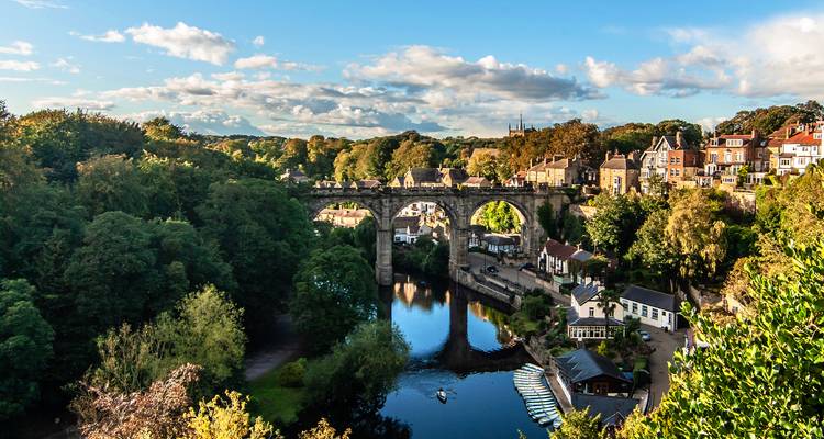 Steinerne Eisenbahnviadukt überspannt eine bewaldete Schlucht mit einem ruhigen Fluss und der charmanten Dorfumgebung von Harrogate.