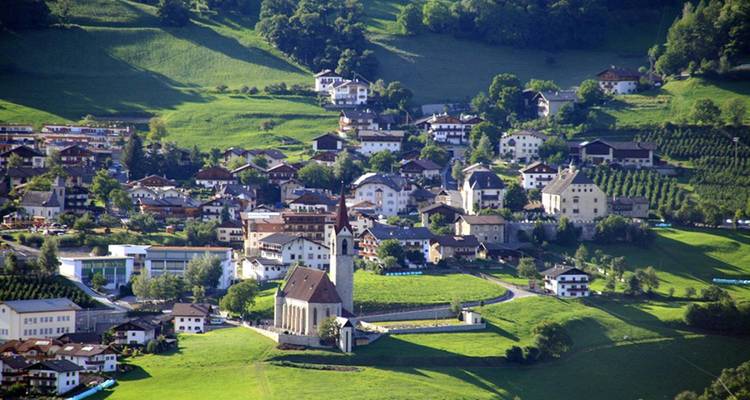 Groene Zuid-Tiroolse heuvel vol traditionele alpine huisjes en een kerkspits.