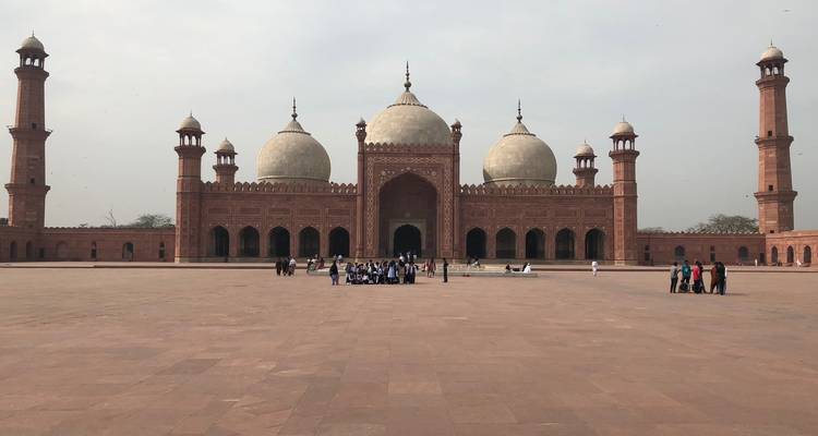 Ruim uitzicht op de binnenplaats van de Badshahi Moskee met bezoekers in de buurt van de indrukwekkende structuur uit het Mughal-tijdperk.