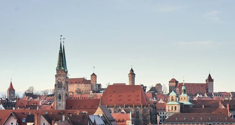 Vue du toit de Nuremberg avec des toits de tuiles rouges, des clochers d'église et des tours médiévales sous un ciel dégagé.