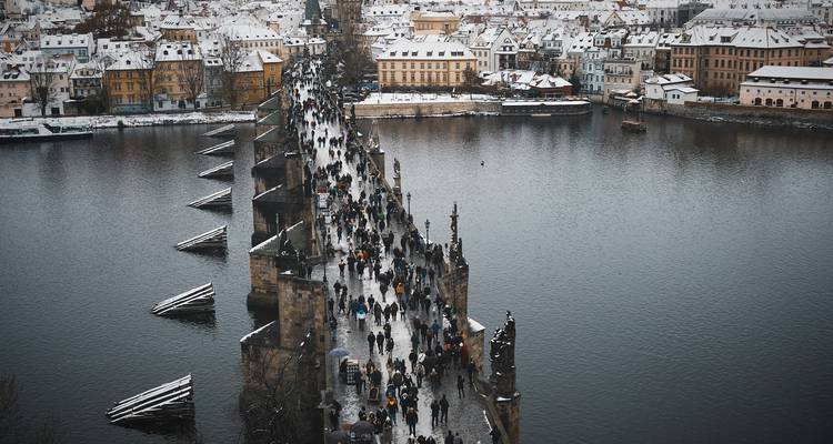 Panorama enneigé de Prague présentant le pont Charles très fréquenté enjambant la rivière Vltava.