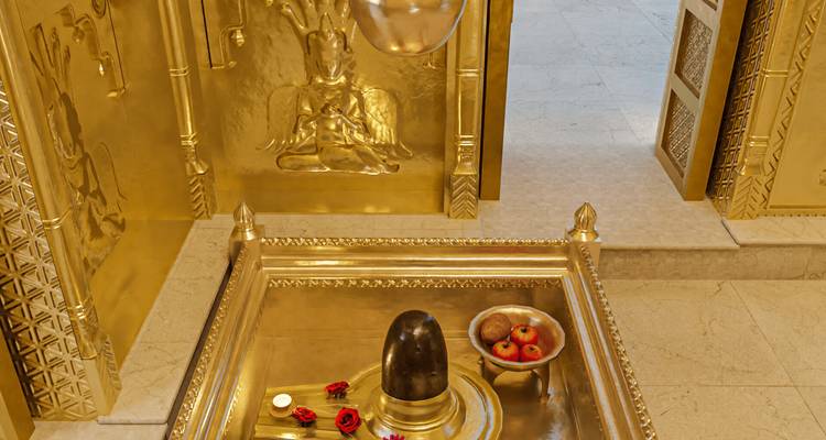 Sanctuaire intérieur luxueux plaqué or avec un lingam de Shiva noir orné de roses rouges et d'offrandes.