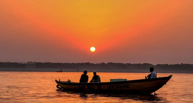Des bateliers en silhouette glissent sur le Gange au lever du soleil, le ciel rougeoyant d'orange au-dessus des eaux calmes.