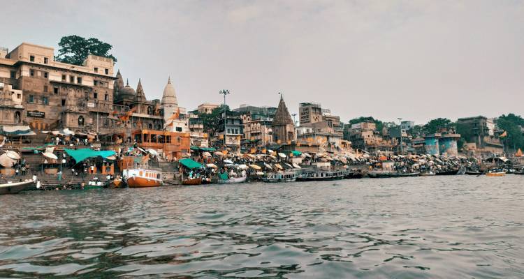 Les ghats iconiques de Varanasi bordés de temples et de bâtiments s'élevant au-dessus du Gange tandis que des bateaux flottent à proximité.