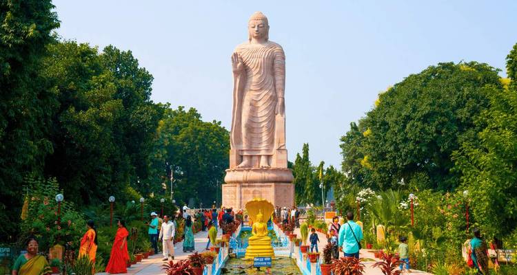 Statue massive de Bouddha debout dominant une allée de jardin paysager remplie de pèlerins et de visiteurs.