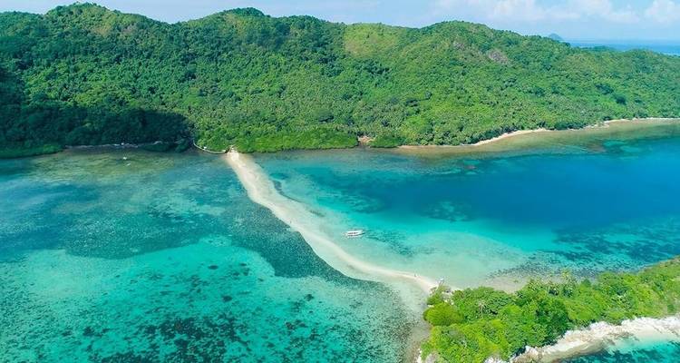 Aerial view of a winding white sandbar separating vibrant turquoise shallows from deeper blue lagoon and forested hills.