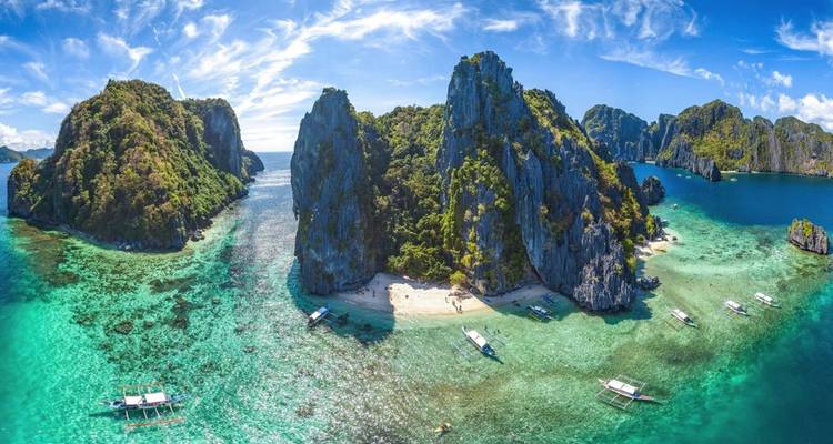 Spectacular karst limestone islands and turquoise lagoons of El Nido seen from above with outrigger boats moored on a tiny beach.