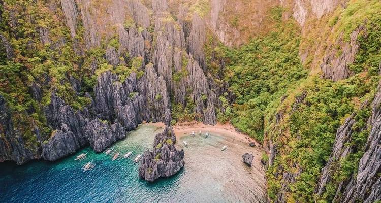 Secluded pocket beach fringed by towering jagged limestone walls and lush forest in El Nido.