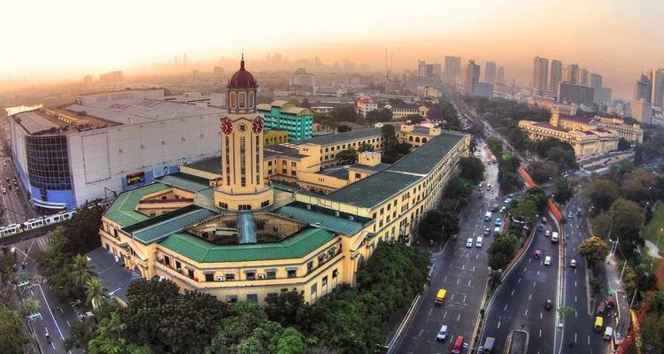 Aerial shot of Manila City Hall’s clock tower surrounded by busy highways and hazy urban skyline at dawn.