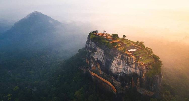 Dramatic aerial of Sigiriya rock fortress rising above misty jungle at sunrise