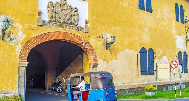 Blue tuk-tuk driving through an old yellow colonial archway in Galle Fort