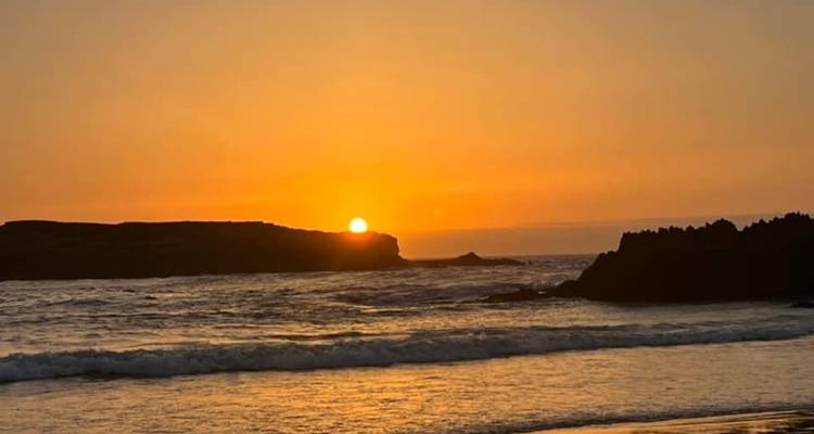 El sol se pone sobre el Atlántico, proyectando luz dorada sobre las olas y los afloramientos rocosos.