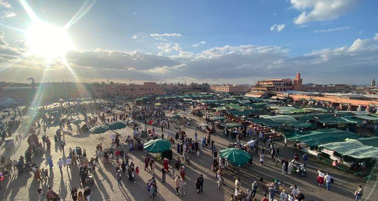 Las multitudes llenan una vasta plaza de mercado bordeada de toldos verdes bajo un sol bajo de la tarde.