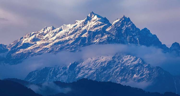 Der schneebedeckte Gipfel des Kanchenjunga erhebt sich bei Tagesanbruch über Schichten nebelverhangener Bergkämme.