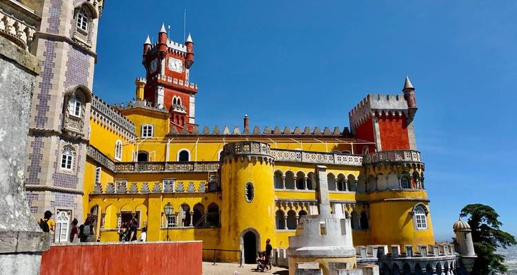 Leuchtend gelbe und rote Fassaden des Pena-Palastes erheben sich gegen einen klaren blauen Himmel in Sintra.