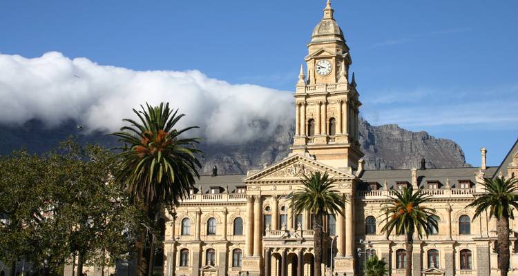 Hôtel de ville historique du Cap avec tour de l'horloge encadré par des palmiers et les nuages de Table Mountain.