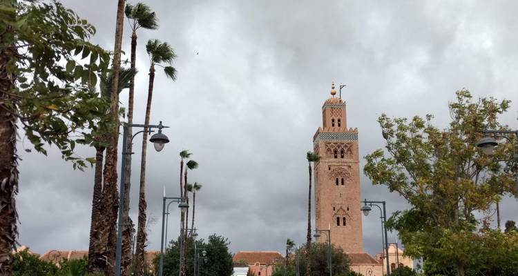 Das Minarett der Koutoubia-Moschee ragt über Palmen unter einem düsteren grauen Himmel in Marrakesch empor.