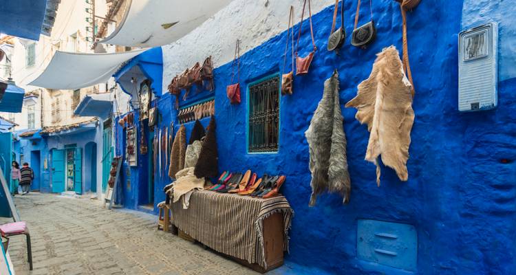 Lebendige blaue Gasse in Chefchaouen mit Lederwaren und Kunsthandwerk, die an weiß getünchten Wänden hängen.