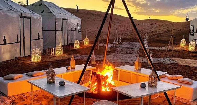 Wüsten-Glamping-Camp in der Dämmerung mit laternenbeleuchteten Zelten um ein knisterndes zentrales Lagerfeuer.