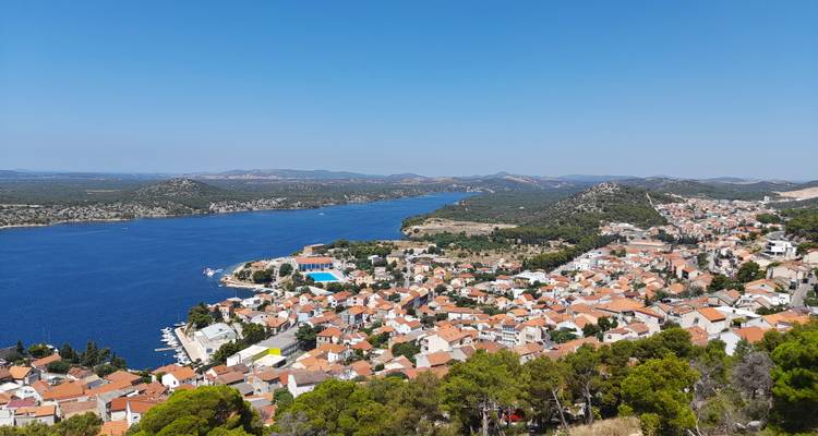 Point de vue élevé surplombant une ville côtière croate aux toits de tuiles rouges bordant une baie bleu profond et des collines boisées sous un ciel dégagé.