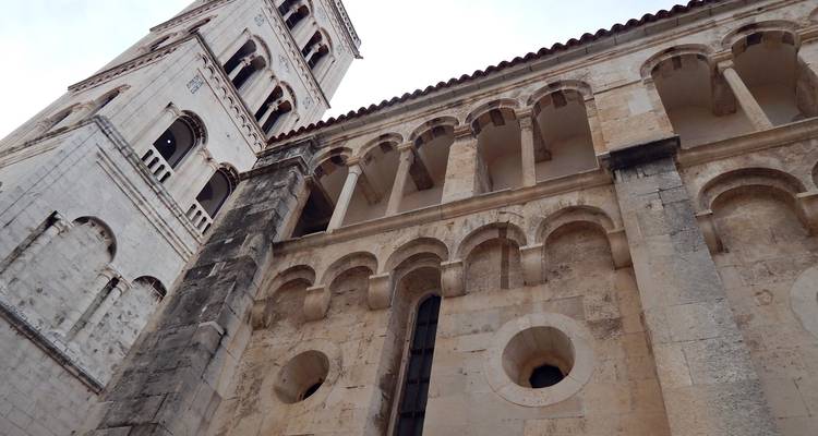 Angle ascendant d'un clocher en pierre et arcs romans d'une cathédrale historique contre un ciel partiellement nuageux.
