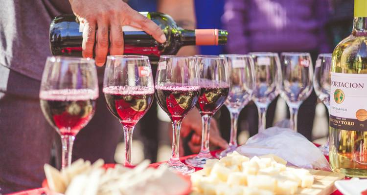 Close-up of red wine being poured into several glasses on a table with cubes of cheese.