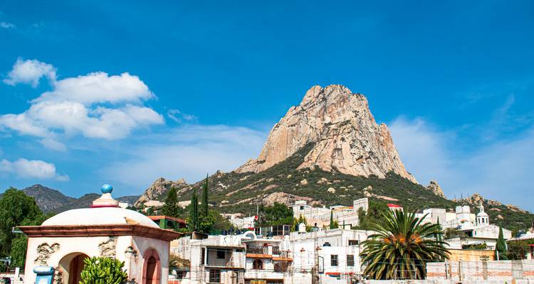 Peña de Bernal monolith towering over a small Mexican town beneath a clear blue sky.