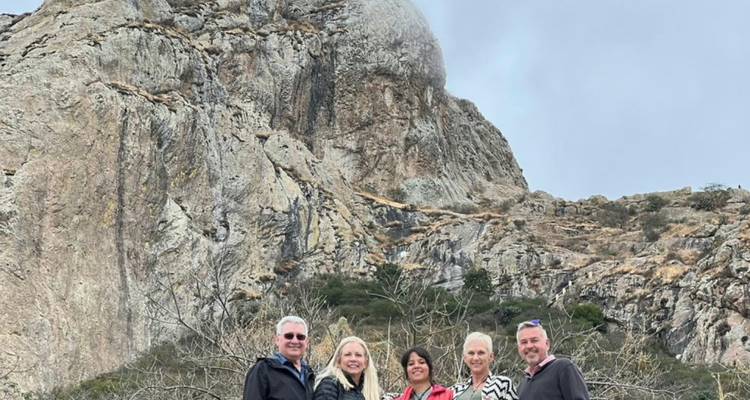 Five travelers pose in front of a steep rocky mountain cliff.