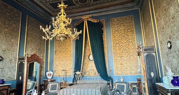 Weelderige historische slaapkamer met sierlijke kroonluchter, goudgeaccentueerde blauwe muren en antieke meubels.