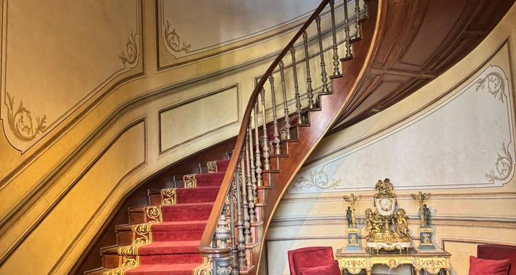 Elegante gebogen houten trap met rood tapijt en sierlijke wanddetaillering in een landhuis.