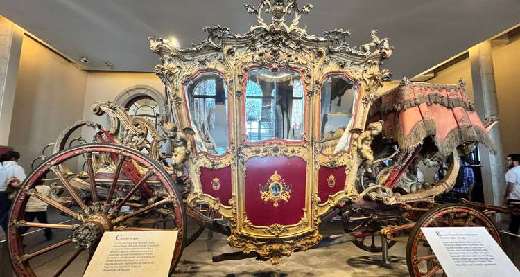 Vergulde paardenkoets tentoongesteld in een museumzaal met bezoekers die toekijken.